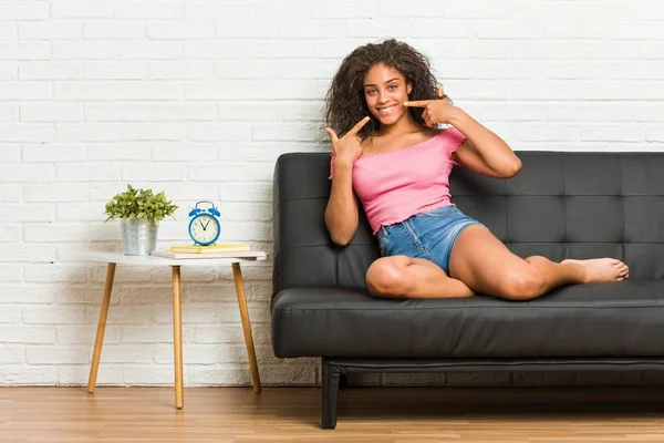 坐在沙发上的年轻的非洲裔美国女人笑着 用手指捂住嘴 — 图库照片