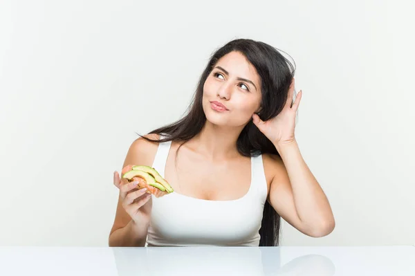 Young Hispanic Woman Holding Avocado Toast Trying Listening Gossip — Stock Photo, Image