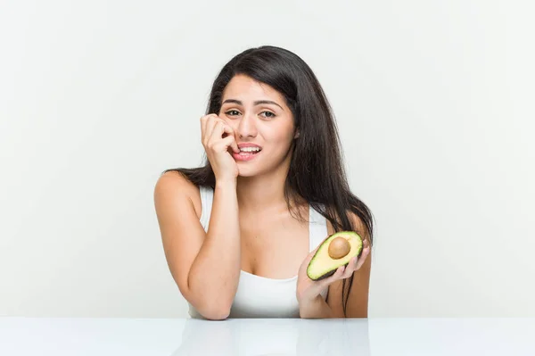 Mujer Hispana Joven Sosteniendo Aguacate Mordiéndose Las Uñas Nerviosa Muy — Foto de Stock