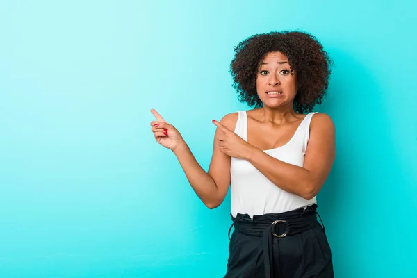 Young african american woman shocked pointing with index fingers to a copy space.