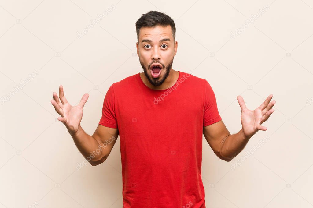 Young south-asian man celebrating a victory or success, he is surprised and shocked.