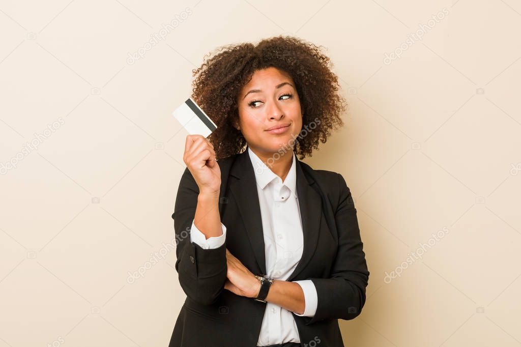 Young african american woman holding a credit card looking sideways with doubtful and skeptical expression.