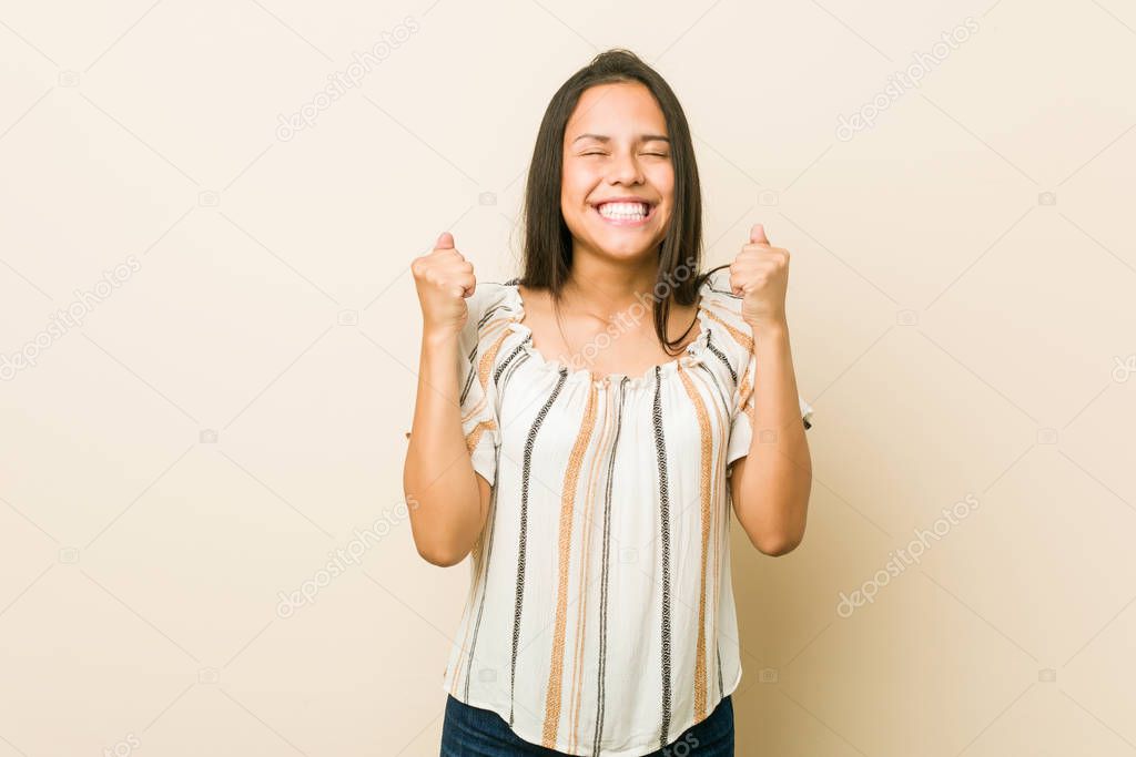 Young hispanic woman raising fist, feeling happy and successful. Victory concept.