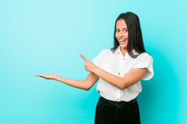 Mavi bir duvara yaslanmış genç, Latin asıllı, havalı bir kadın. Elinde bir fotokopi odası tutuyor..