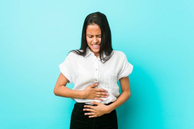 Genç İspanyol asıllı havalı kadın mavi bir duvara karşı hasta, karın ağrısı çeken, acı verici hastalık konsepti olan.