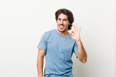 Beyaz arka planda genç yakışıklı bir adam göz açıp kapayıncaya kadar iyi bir el hareketi yapıyor..