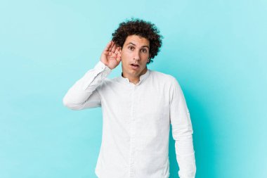 Genç, kıvırcık, olgun bir adam zarif bir gömlek giyip bir dedikoduyu dinlemeye çalışıyor..