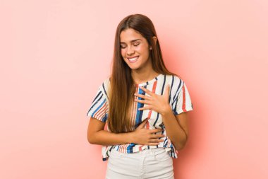 Genç sıska kadın mutlu bir şekilde gülüyor ve ellerini karnının üstünde tutarak eğleniyor..