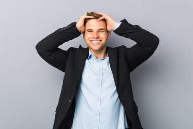 Young handsome caucasian man laughs joyfully keeping hands on head. Happiness concept.