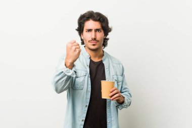 Genç havalı adam kameraya yumruğunu gösteren bir kahve içiyor, agresif yüz ifadesi..