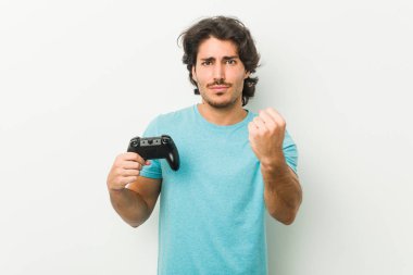 Elinde oyun kumandası olan genç bir adam kameraya yumruğunu gösteriyor, agresif bir yüz ifadesi..