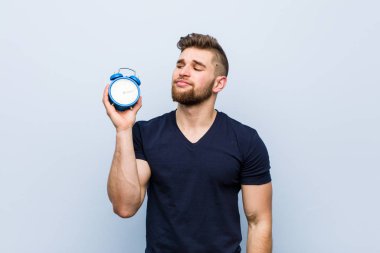 Çalar saati tutan beyaz bir genç şüpheli ve şüpheci bir ifadeyle yana bakıyor..