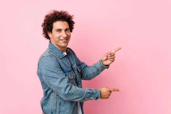 Curly Mature Man Wearing Denim Jacket Pink Background Excited Pointing — ストック写真