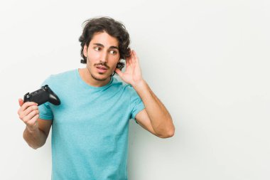 Elinde oyun kumandası olan genç bir adam bir dedikoduyu dinlemeye çalışıyor..