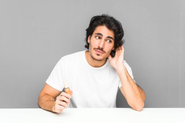 Genç adam sakalını kesiyor. Dedikoduları dinlemeye çalışıyor..