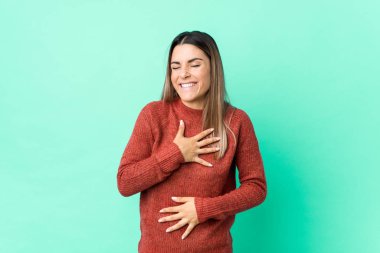 Genç beyaz kadın mutlu bir şekilde gülüyor ve ellerini karnının üstünde tutarak eğleniyor..