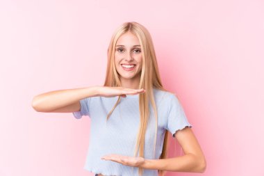 Pembe arka plandaki genç sarışın kadın iki eliyle bir şey tutuyor, ürün sunumu..