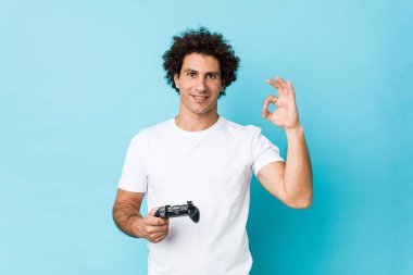 Beyaz, kıvırcık, elinde oyun kumandası olan neşeli ve kendinden emin genç bir adam..