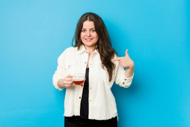 Elinde çay fincanı tutan genç bir kadın tişörtün fotokopi odasını gösteriyor, gururlu ve kendinden emin.