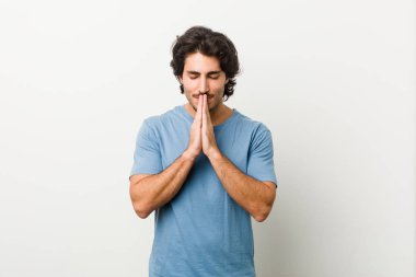 Beyaz arkaplanda el ele tutuşan yakışıklı bir genç. Ağız kenarında dua ediyor. Kendine güveniyor..