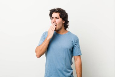 Beyaz bir zemin üzerinde genç yakışıklı bir adam esniyor. Ağzı eliyle kapatan yorgun bir hareket sergiliyor..