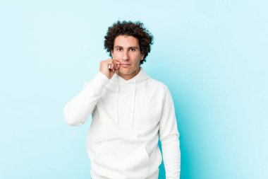 Genç sporcu adam mavi arka planda parmakları dudaklarında bir sır saklıyor..