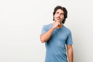 Beyaz bir arka planı olan genç ve yakışıklı bir adam şüpheli ve şüpheci bir ifadeyle yana bakıyor..