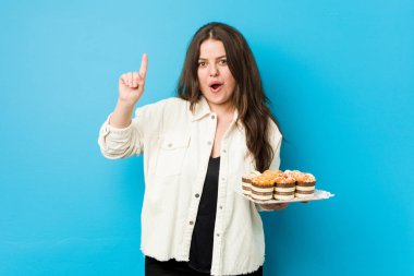 Genç, kıvrımlı bir kadın elinde kek tutuyor. Bir fikri, ilham verici bir fikri var..