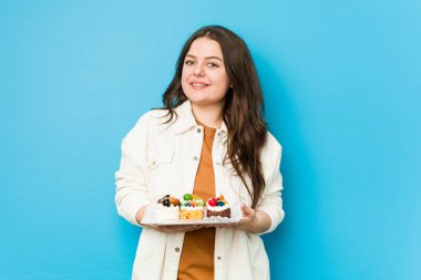 Genç, kıvrımlı bir kadın elinde tatlı bir pasta, mutlu, güler yüzlü ve neşeli.