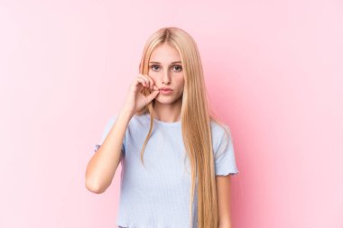 Pembe arka planda, dudakları dudaklarında bir sır saklayan genç sarışın kadın..