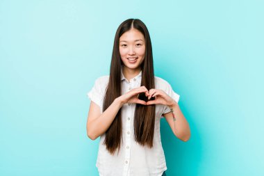 Genç, güzel Çinli kadın gülümsüyor ve elleriyle kalp şeklini gösteriyor..