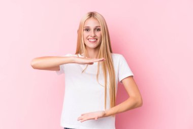 Pembe arka plandaki genç sarışın kadın iki eliyle bir şey tutuyor, ürün sunumu..