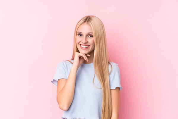 Young blonde woman on pink background smiling happy and confident, touching chin with hand.