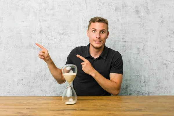 Young Man Holding Sand Timer Table Shocked Pointing Index Fingers — ストック写真
