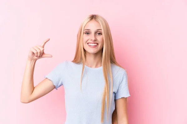 Mladá Blondýnka Růžovém Pozadí Drží Něco Málo Prsty Usmívá Sebevědomě — Stock fotografie