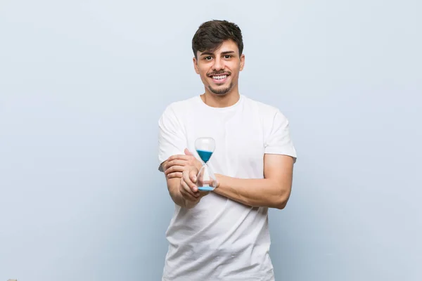 Jonge Spaanse Man Met Een Zandloper Die Vol Zelfvertrouwen Glimlacht — Stockfoto