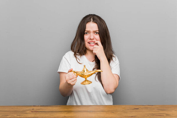 Young plus size curvy woman holding a magic lamp biting fingernails, nervous and very anxious.
