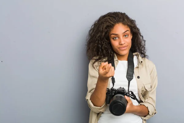 若いアフリカ系アメリカ人の写真家の女性を保持しているカメラを指して指であなたを招待するかのように近づく — ストック写真