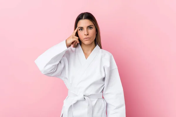 Young karate woman pointing temple with finger, thinking, focused on a task.