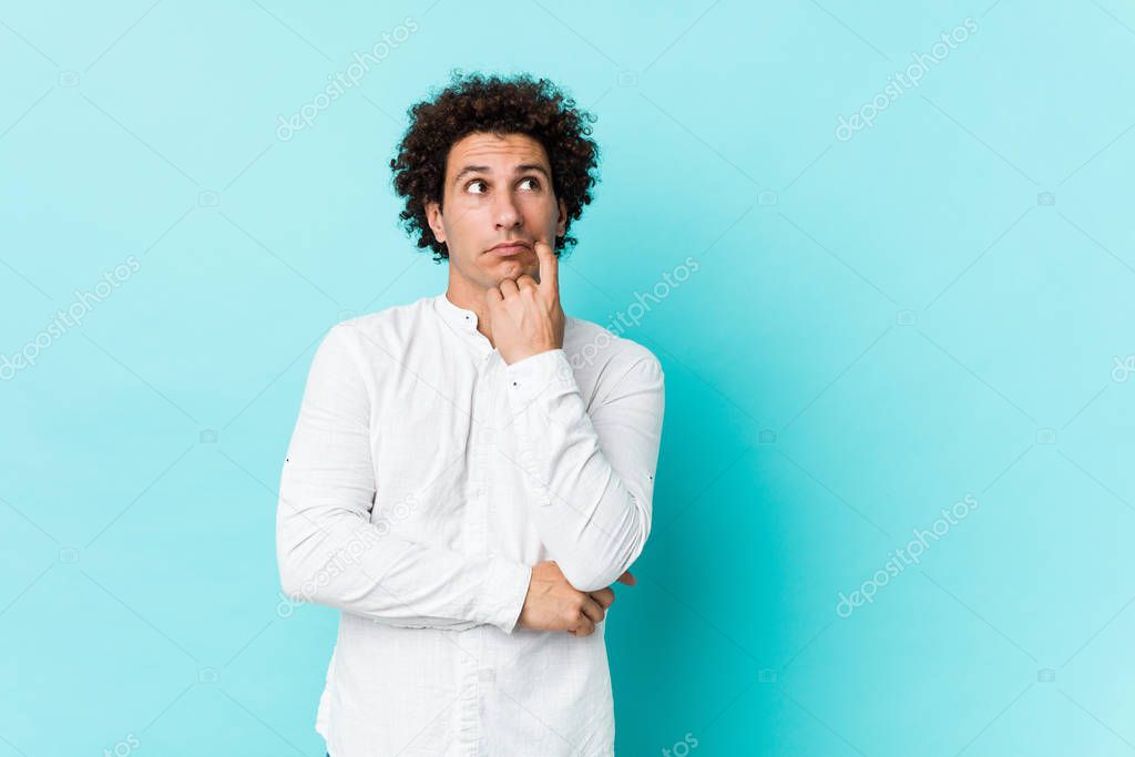 Young curly mature man wearing an elegant shirt relaxed thinking about something looking at a copy space.
