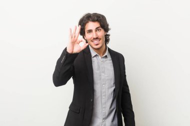 Genç bir iş adamı beyaz bir arka plana karşı neşeli ve kendinden emin iyi bir hareket gösteriyor..