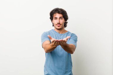 Beyaz arka planda genç yakışıklı bir adam elinde avuç içi bir şeyle kameraya sunuyor..