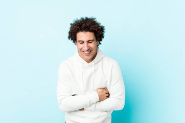 Mavi arka planda genç bir sporcu mutlu bir şekilde gülüyor ve elleri karnında gezdirirken eğleniyor..