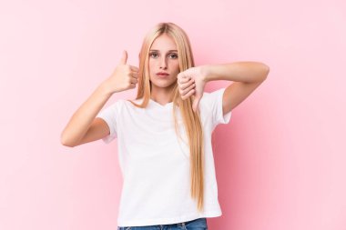 Pembe arka planda genç sarışın kadın baş parmağını kaldırıyor ve baş parmağını eğiyor, zor seçim konsepti.