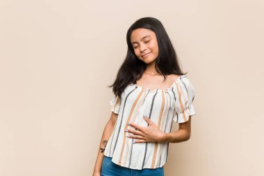 Genç sevimli Çinli genç sarışın kadın pembe arka planda palto giyiyor karnına dokunuyor, hafifçe gülümsüyor, yemek yiyor ve tatmin oluyor..