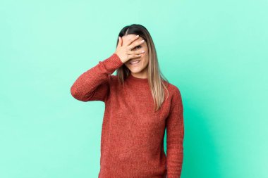 Genç beyaz kadın kameraya parmaklarıyla göz kırpıyor, yüzünü kapatmaktan utanıyor..