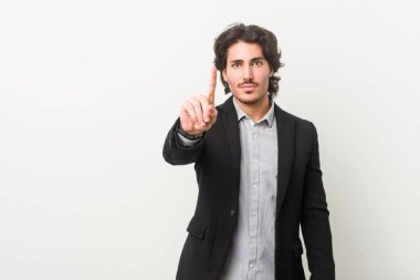 Genç bir iş adamı beyaz arka planda bir numarayı parmaklarıyla gösteriyor..