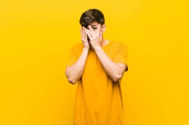 Genç Latin asıllı sıradan bir adam parmaklarının arasından korkmuş ve gergin bir şekilde göz kırpıyor..