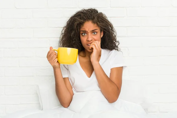 Jovem Afro Americana Sentada Cama Segurando Uma Caneca Café Mordendo — Fotografia de Stock