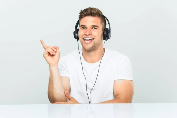 Mladý Muž Poslouchá Hudbu Sluchátky Vesele Usmívá Ukazováčkem Pryč — Stock fotografie